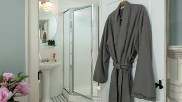 A bathroom with a white sink, a glass shower enclosure, and a robe hanging on a door.