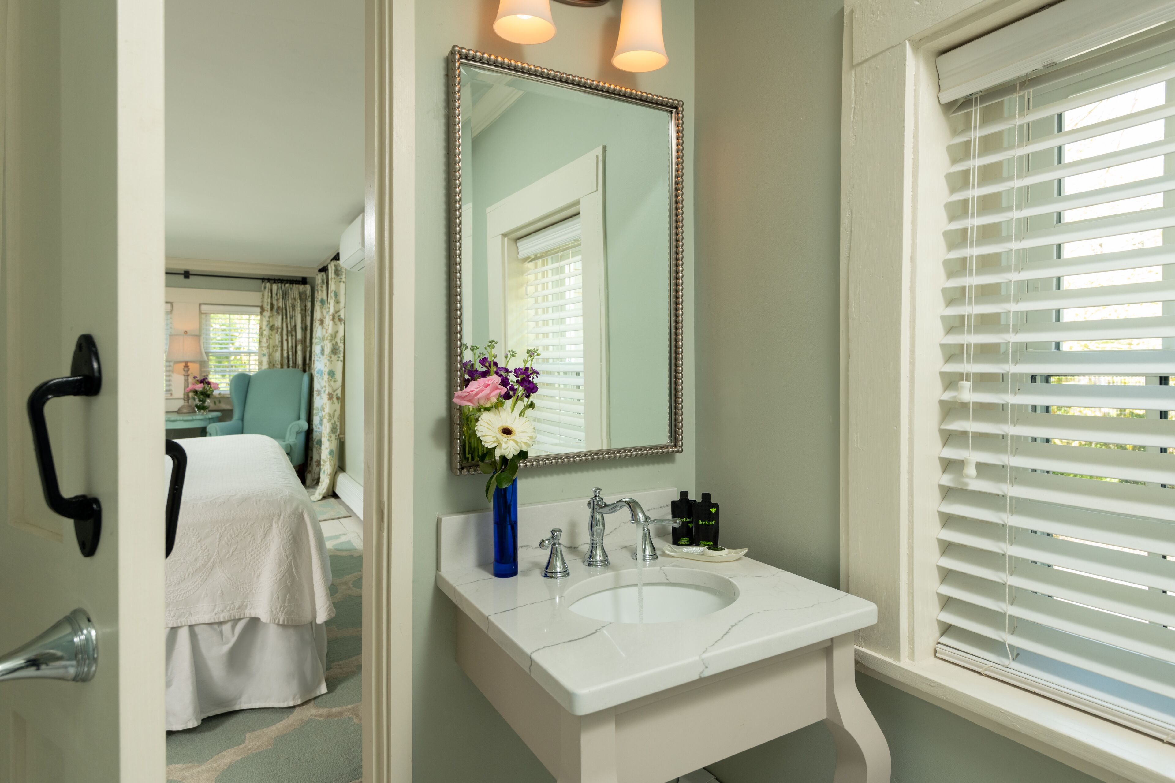 A bathroom with a white sink, a mirror, and a window with blinds.