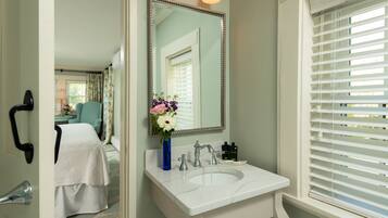 A bathroom with a white sink, a mirror, and a window with blinds.