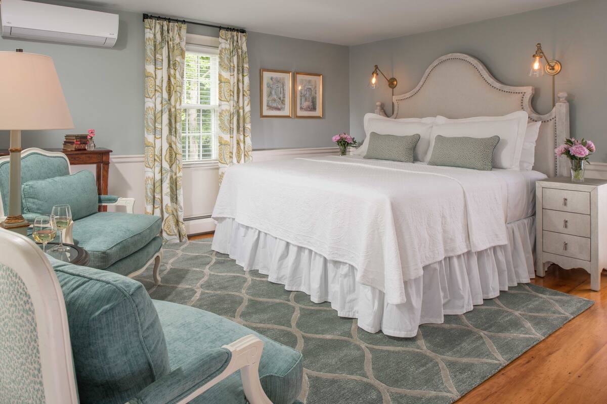 A bedroom with a large bed, a chair, a nightstand, and a window with curtains.