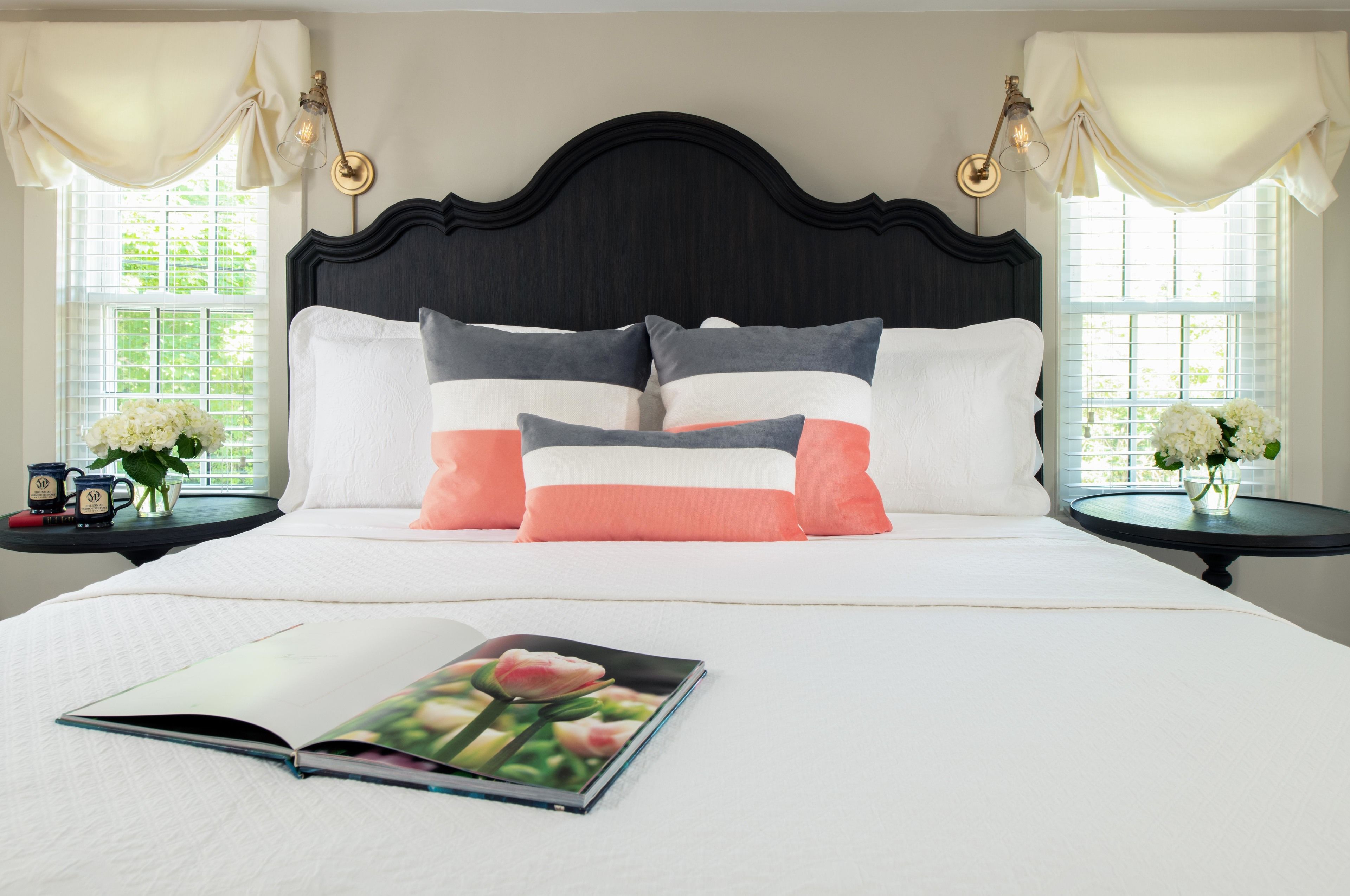 Een opgemaakt bed met een boek erop, twee nachtkastjes met lampen, en een raam met gordijnen.
