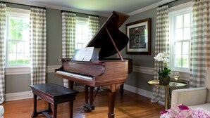 A grand piano in a room with a wooden floor, checkered curtains, and a framed painting on the wall. - The Inn at Yarmouth Port (Yarmouth Port)