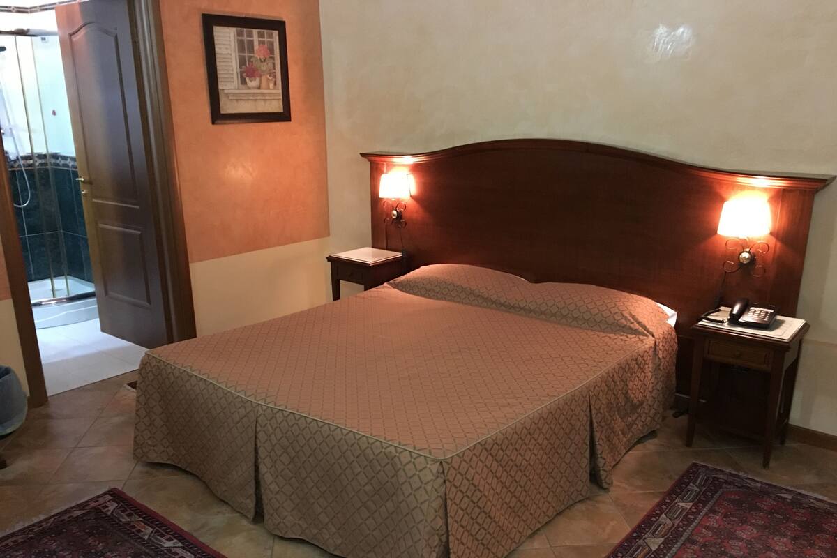 A neatly made bed with a patterned bedspread, a bedside table with a lamp, and a nightstand with a phone.