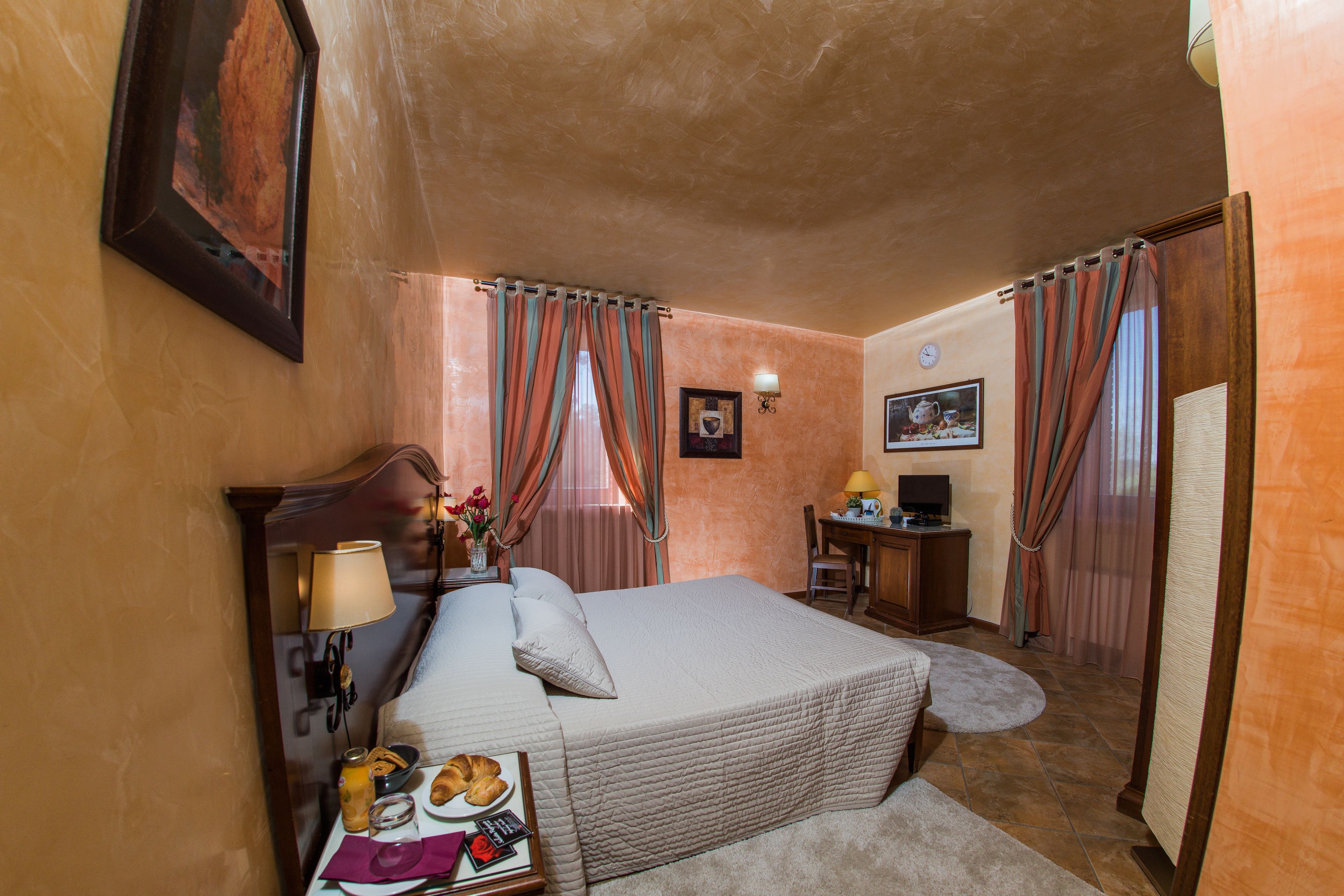 Habitación de hotel con cama, escritorio, silla, lámpara, un cuadro y cortinas.