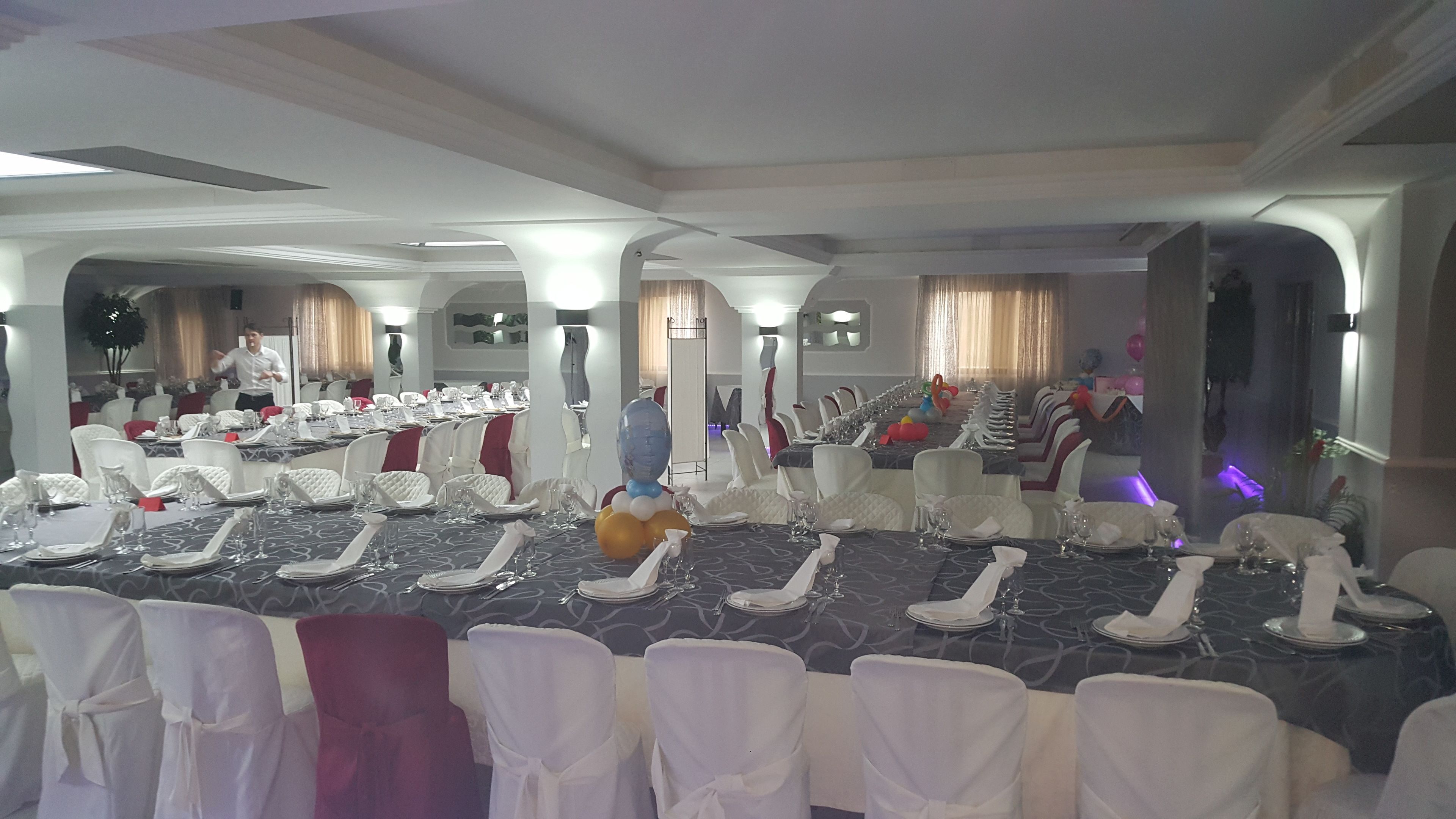 A banquet hall with long tables set for a formal event, white chairs, and a person in the background.