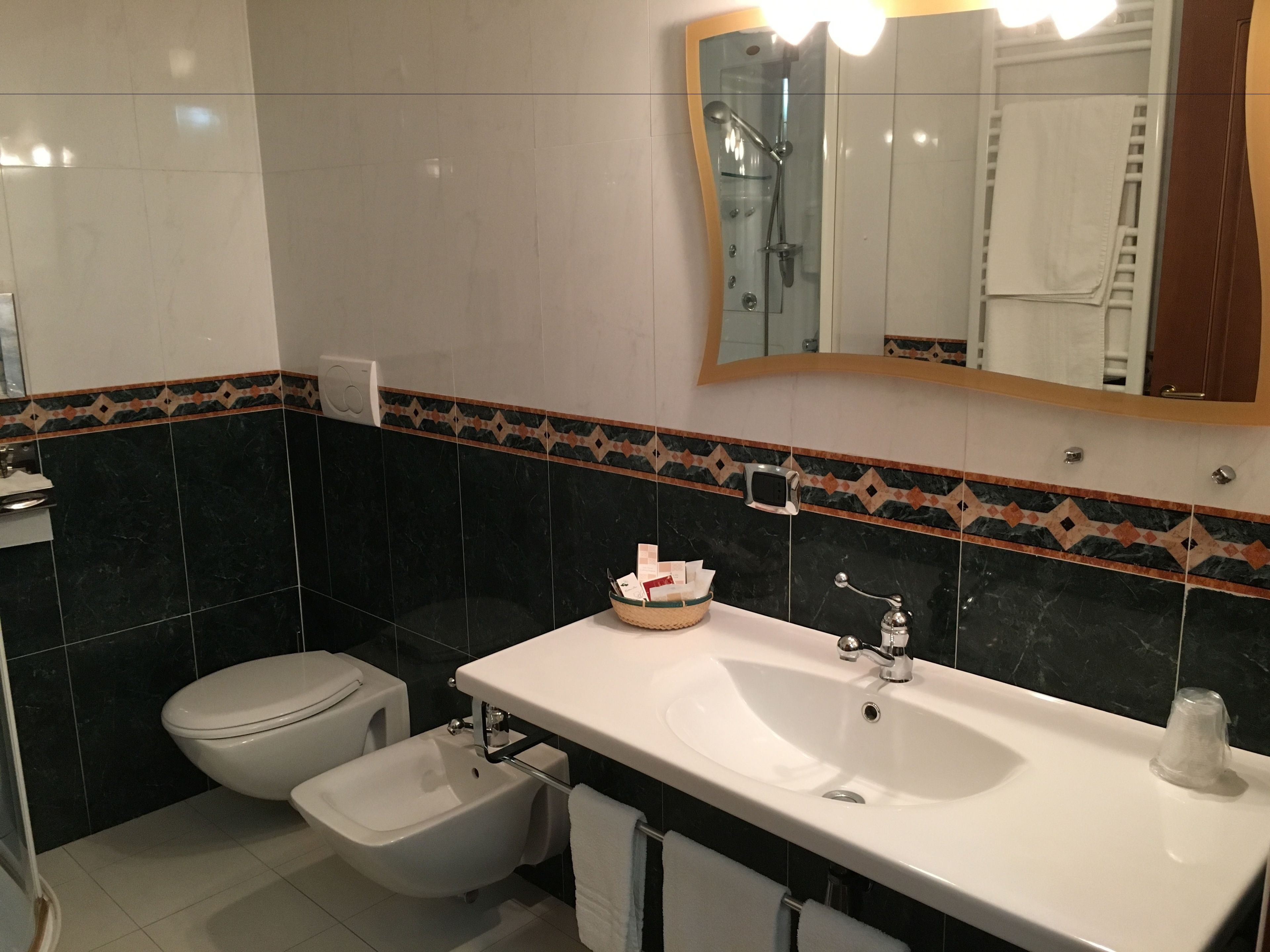 Une salle de bain avec un lavabo blanc, un bidet, des toilettes et un miroir, ainsi qu’une serviette accrochée au mur.