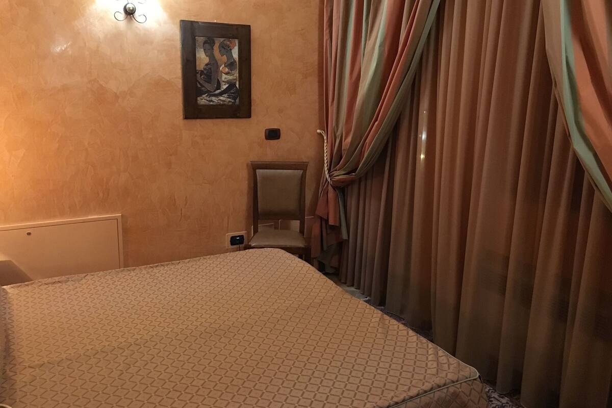 A hotel room with a bed, a chair, a painting on the wall, and curtains.