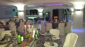 A formal dining room with tables set for a meal, candles, and a bar area in the background. - Hotel Al Ritrovo (Piazza Armerina)