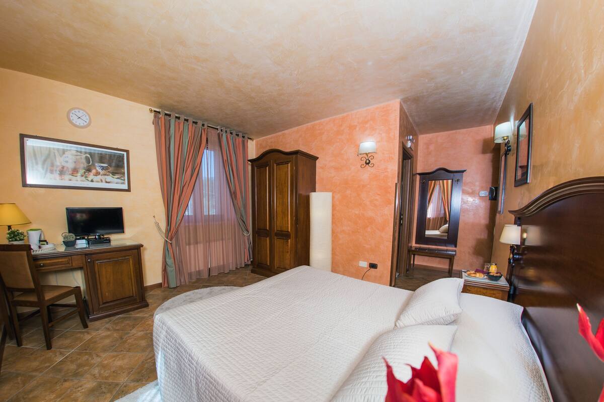 A hotel room with a bed, desk, television, and a painting on the wall.