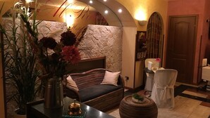 A cozy room with a bed, a small table with a vase of flowers, a chair, and a decorative wall with a mirror. - Hotel Al Ritrovo (Piazza Armerina)