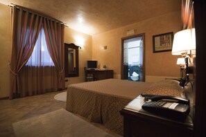 A hotel room with a bed, a desk with a lamp, a television, and a door leading to a balcony.