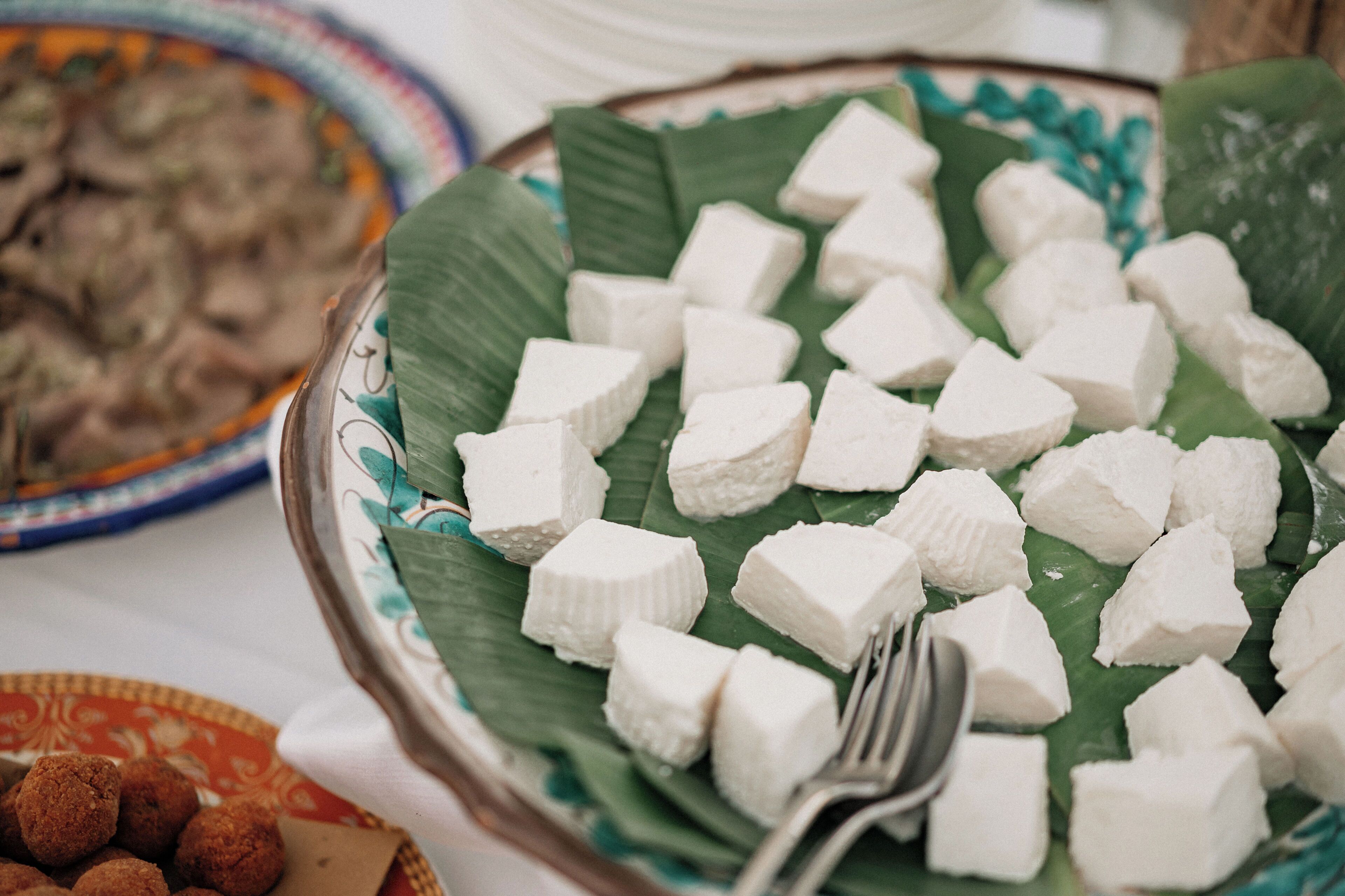 A plate of white cubes on a banana leaf with a fork beside it.