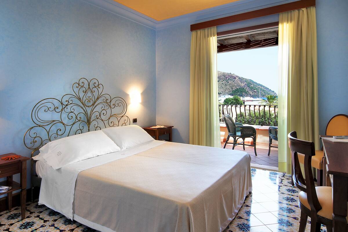 A hotel room with a bed, a desk, a chair, and a view of the outdoors.