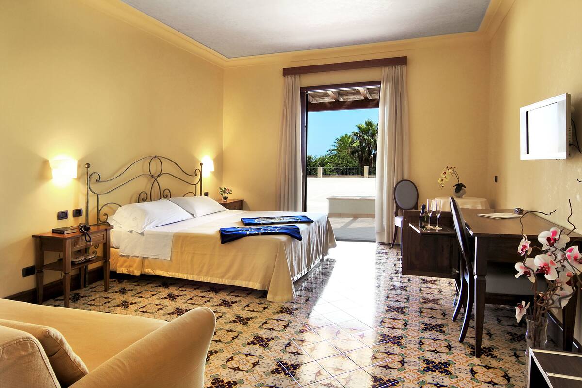 A hotel room with a bed, a desk, a chair, a TV, and a view of the outdoors.