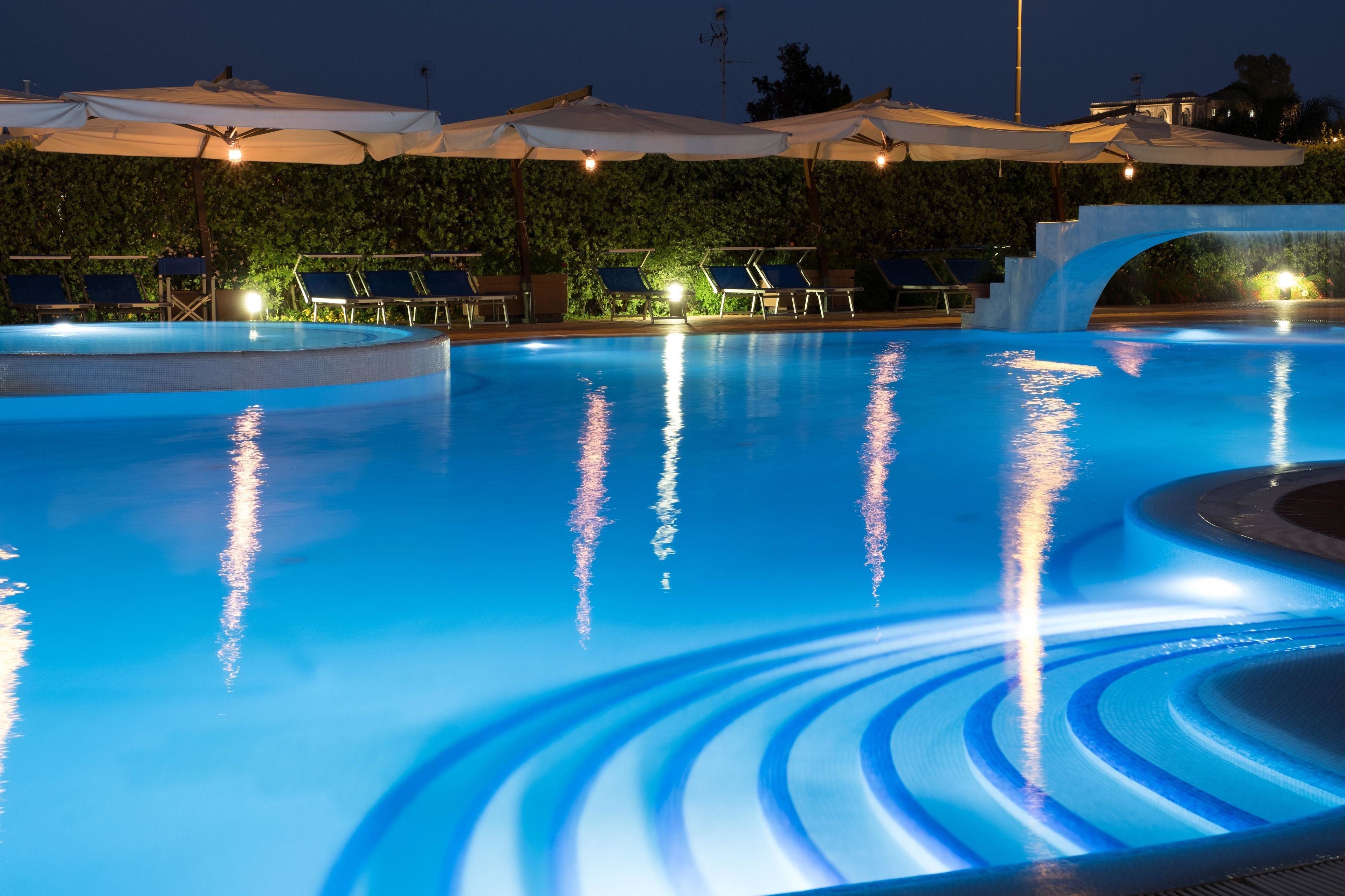 Une piscine entourée d’une haie, avec des chaises longues et des parasols.