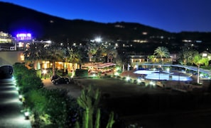 A resort with a swimming pool, outdoor dining area, and a building with illuminated windows.