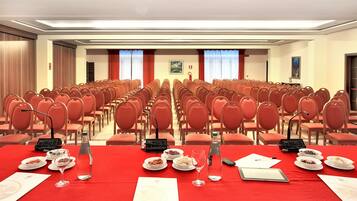 A conference room with rows of red chairs, a table with plates of food, glasses, and a microphone.