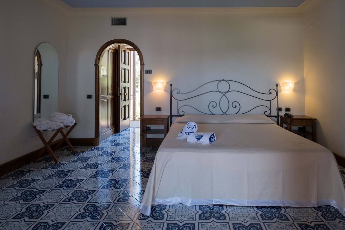 A hotel room with a bed, a mirror, and a tiled floor.