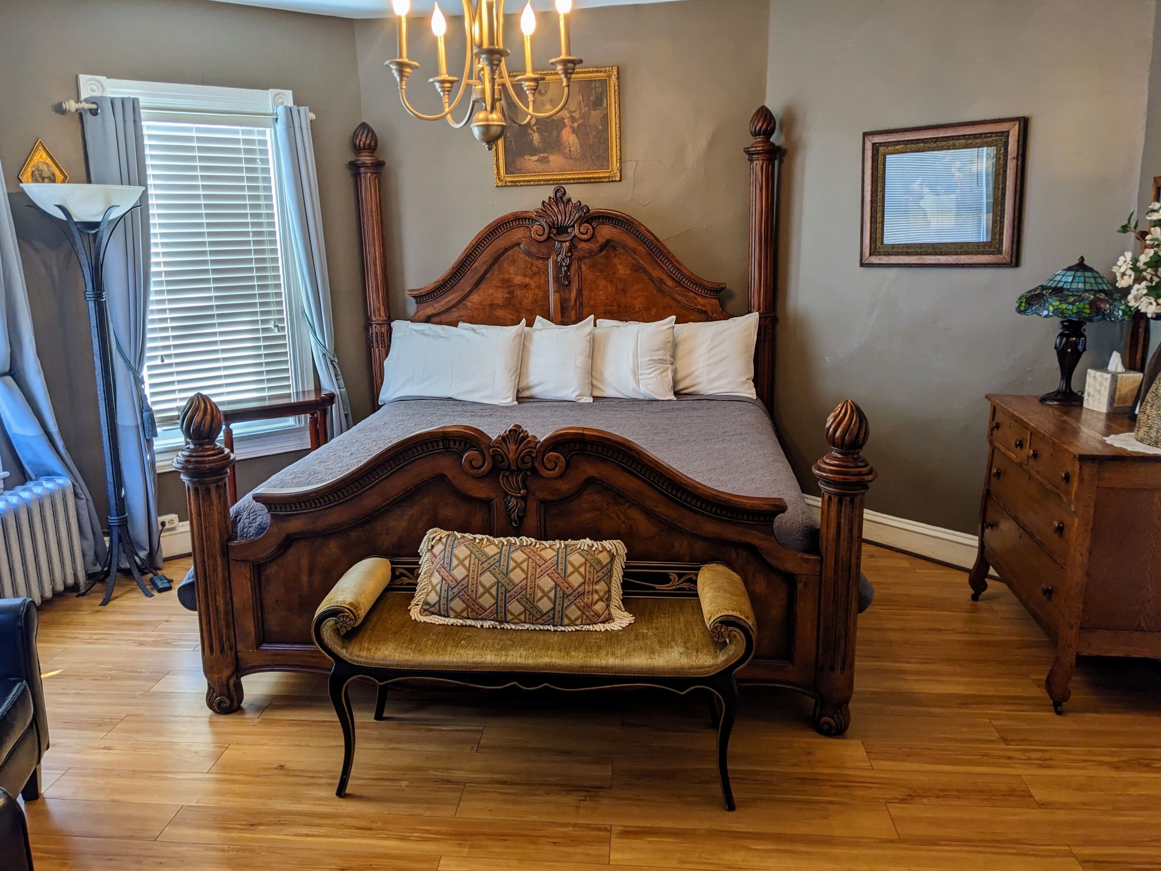 Een slaapkamer met een groot houten bed, een bankje, een kroonluchter en een kaptafel.