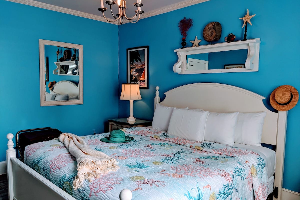 A bedroom with a bed, a nightstand, a lamp, a mirror, and wall decorations.