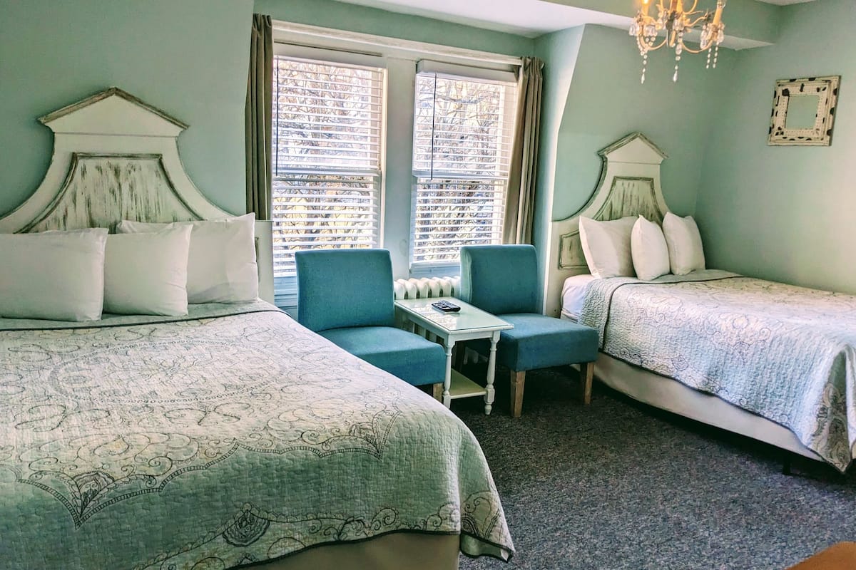 A room with two beds, a chair, a small table, and a chandelier.