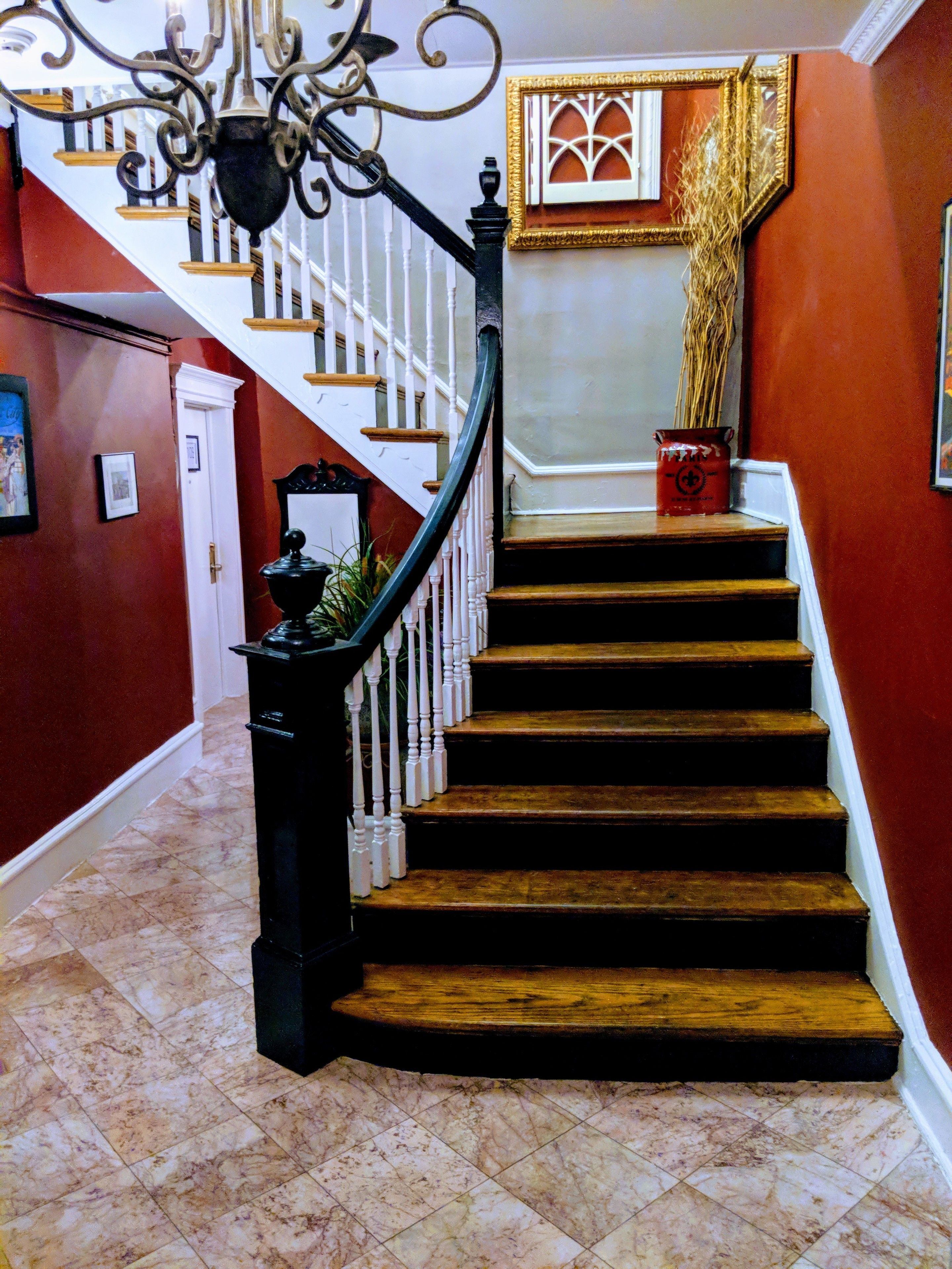 A staircase with a black handrail and white balusters, leading to a landing with a decorative window and a vase on the floor.