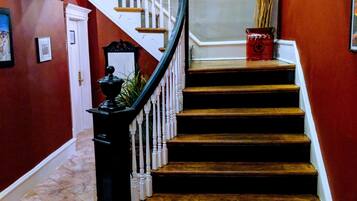 A staircase with a black handrail and white balusters, leading to a landing with a decorative window and a vase on the floor.