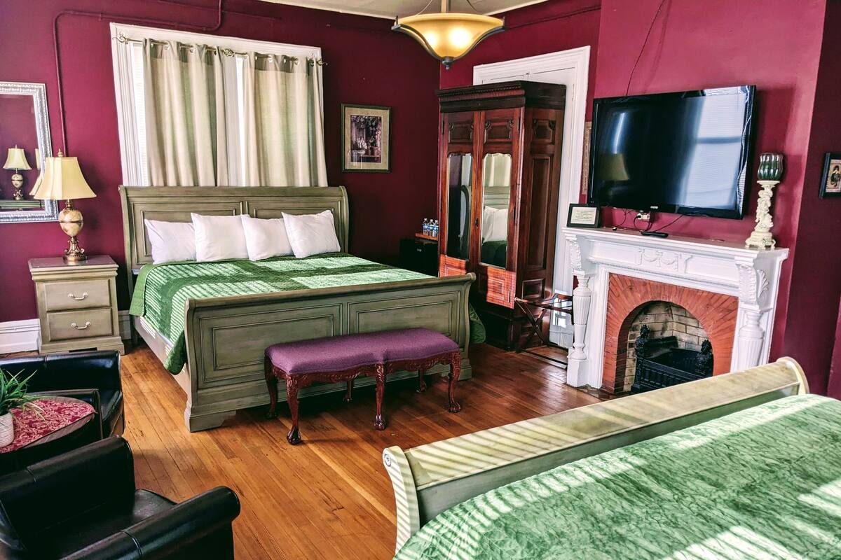 A room with a bed, a bench, a television, a fireplace, and a mirror.