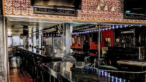 A bar with a tiled wall, a TV mounted above the bar, and a chair with a red cushion.
