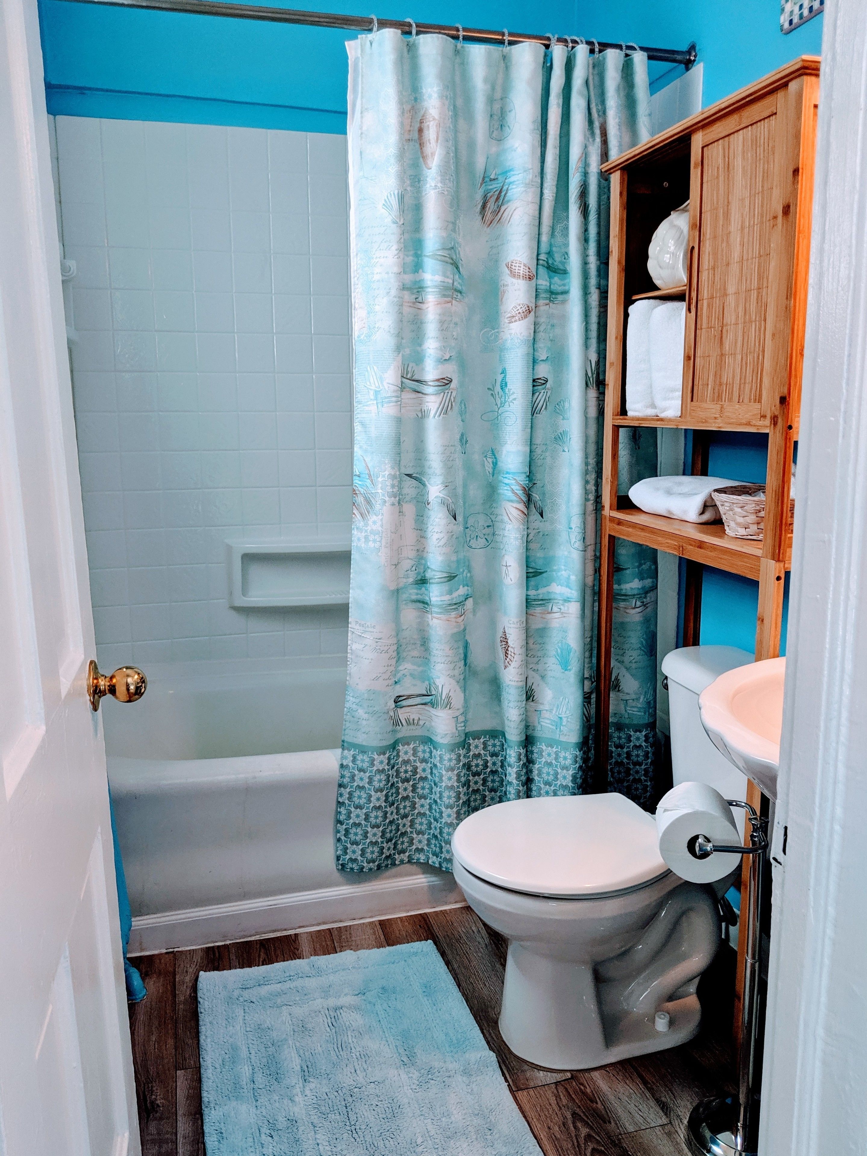 A bathroom with a shower, toilet, and a wooden shelf with towels.