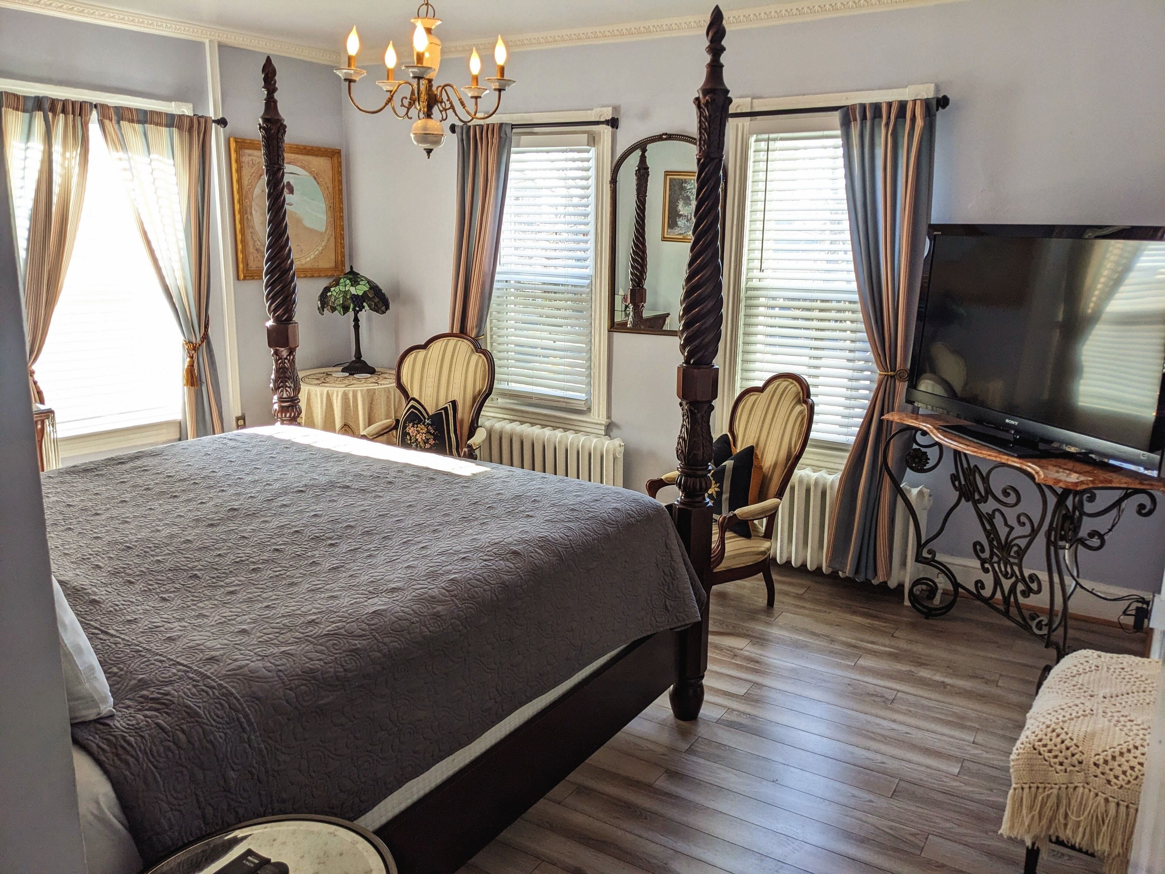 A bedroom with a large bed, a television, a chair, and a desk.