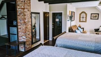 A bedroom with two beds, a brick wall, a wooden bench, a mirror, and a door.