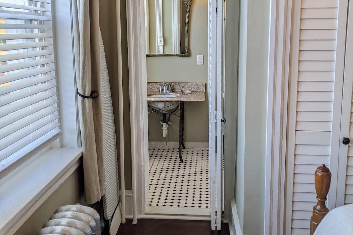 A narrow hallway leading to a bathroom with a sink, a mirror, and a door.