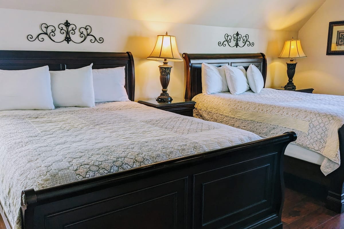 Two double beds with dark wooden frames, white bedding, and decorative wall sconces.