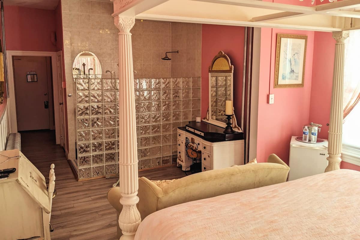 A bedroom with a four-poster bed, a vanity with a mirror, and a window with curtains.