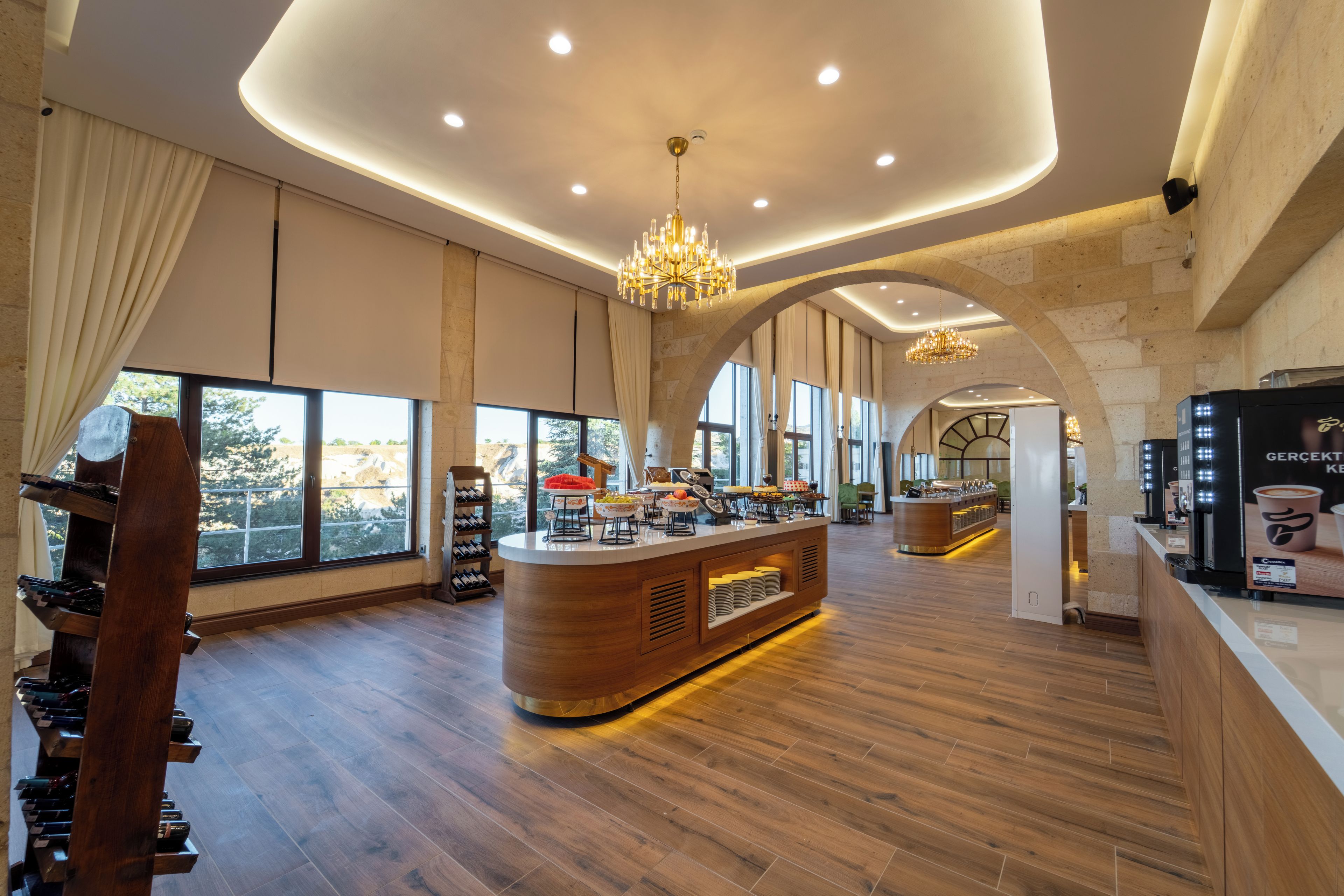 A spacious hotel lobby with a central bar area, large windows, and a wooden floor.