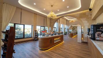 A spacious hotel lobby with a central bar area, large windows, and a wooden floor.
