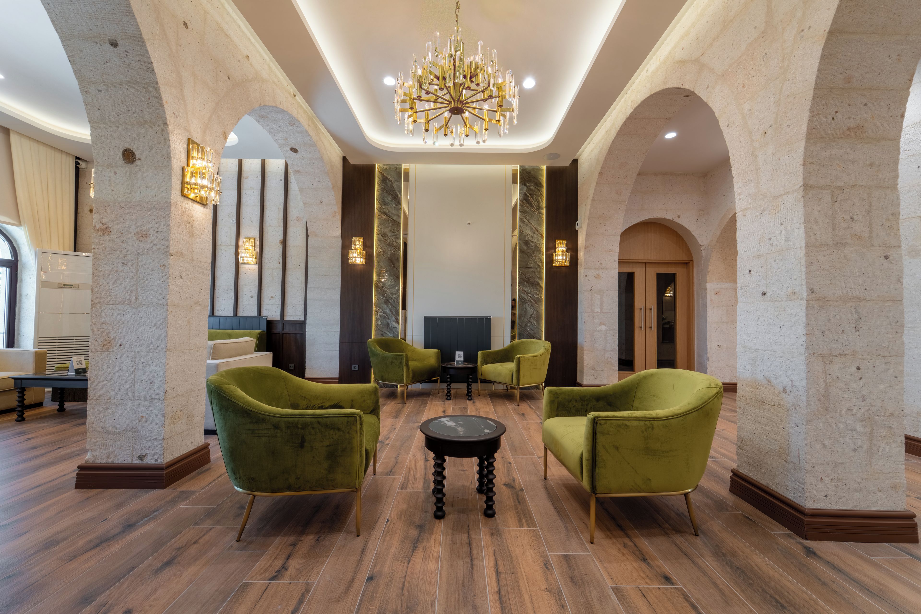 Eine Lobby mit einer Kronleuchter, grünen Polstersesseln, einem schwarzen Couchtisch und einem Fernseher.