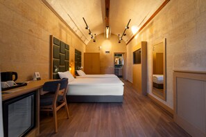 A hotel room with a wooden floor, a desk with a chair, a bed with white bedding, and a large mirror on one wall. - Uchisar Kaya Hotel - Special Class (Nevsehir)