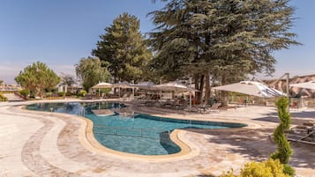 Un área de piscina con diseño curvo, sillas de descanso, sombrillas y árboles.