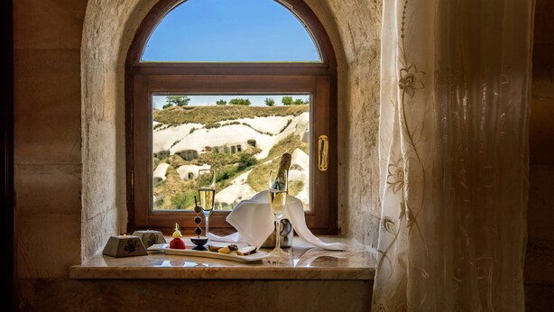 A window with a view of a hilly landscape, a bottle of champagne, and a knife on a table. - Uchisar Kaya Hotel - Special Class (Nevsehir)