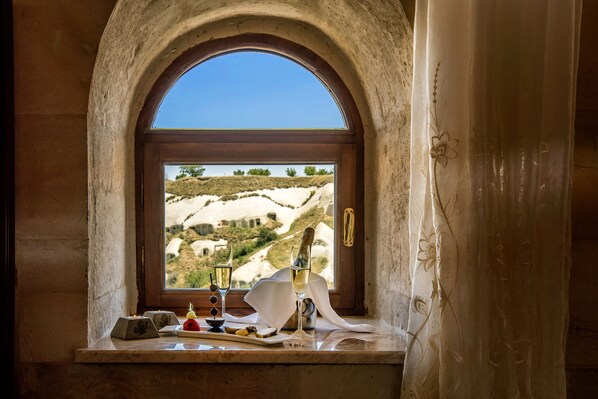 A window with a view of a hilly landscape, a bottle of champagne, and a knife on a table. - Uchisar Kaya Hotel - Special Class (Nevsehir)