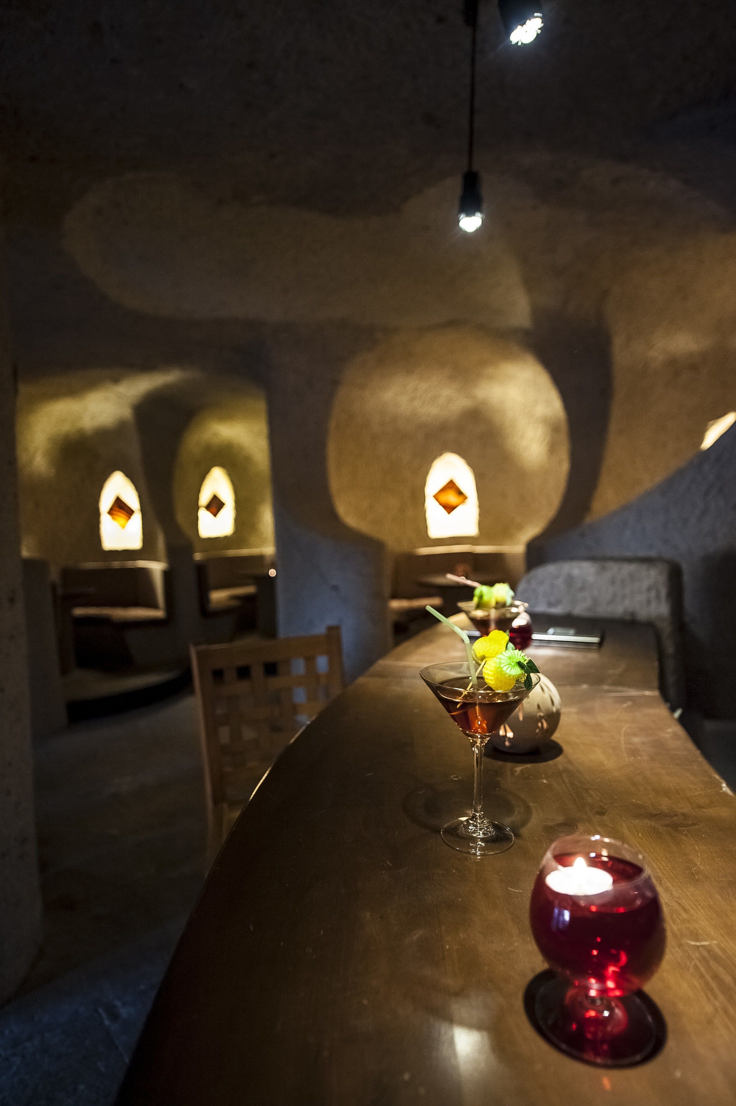 Une pièce faiblement éclairée, avec une longue table, des bougies et un verre à martini garni d’une tranche de citron.