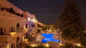 A nighttime view of a hotel with a swimming pool, arched balconies, and a view of the city in the background. - Uchisar Kaya Hotel - Special Class (Nevsehir)