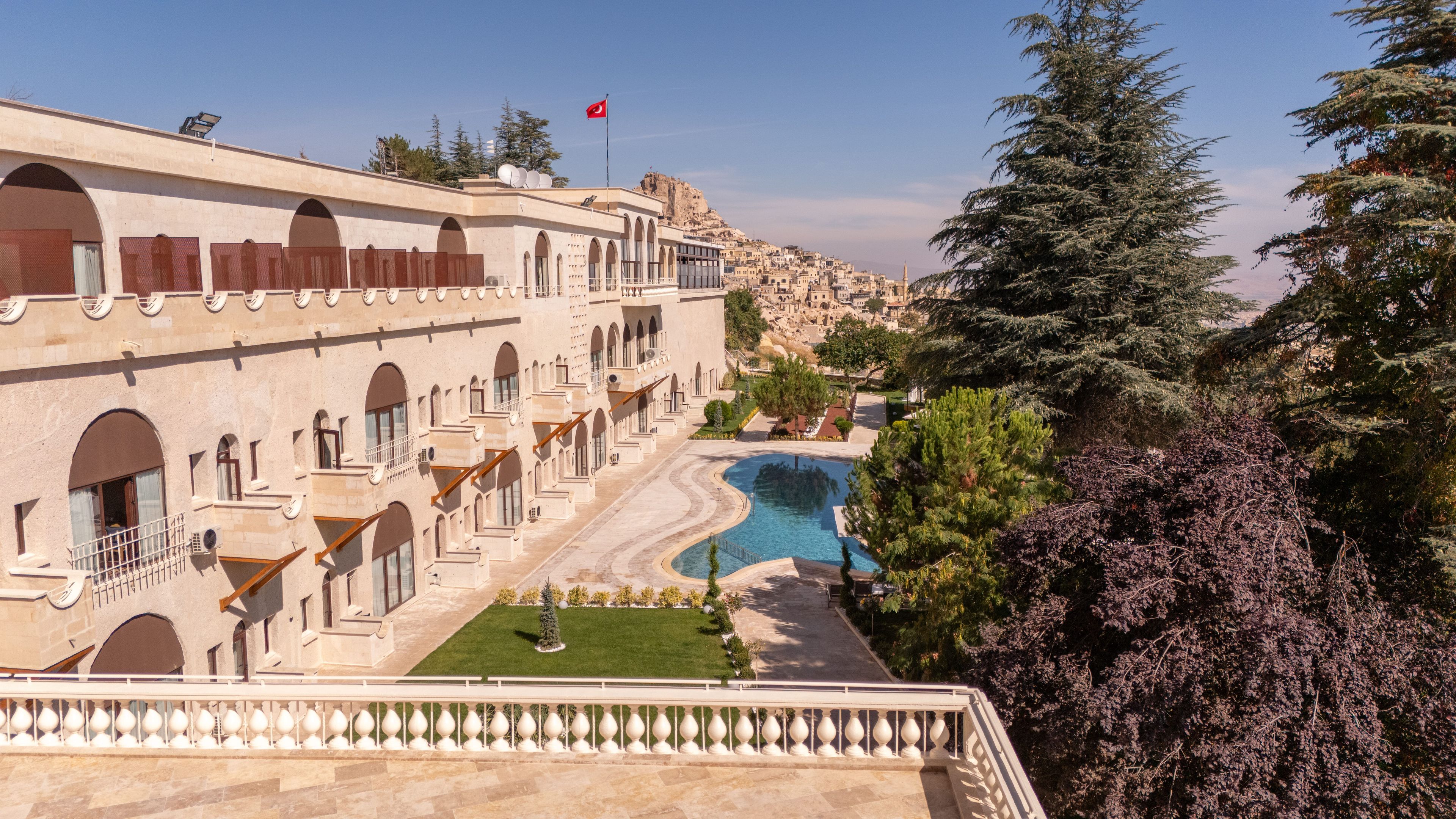 A hotel with multiple balconies, a swimming pool, and a view of a mountainous landscape.