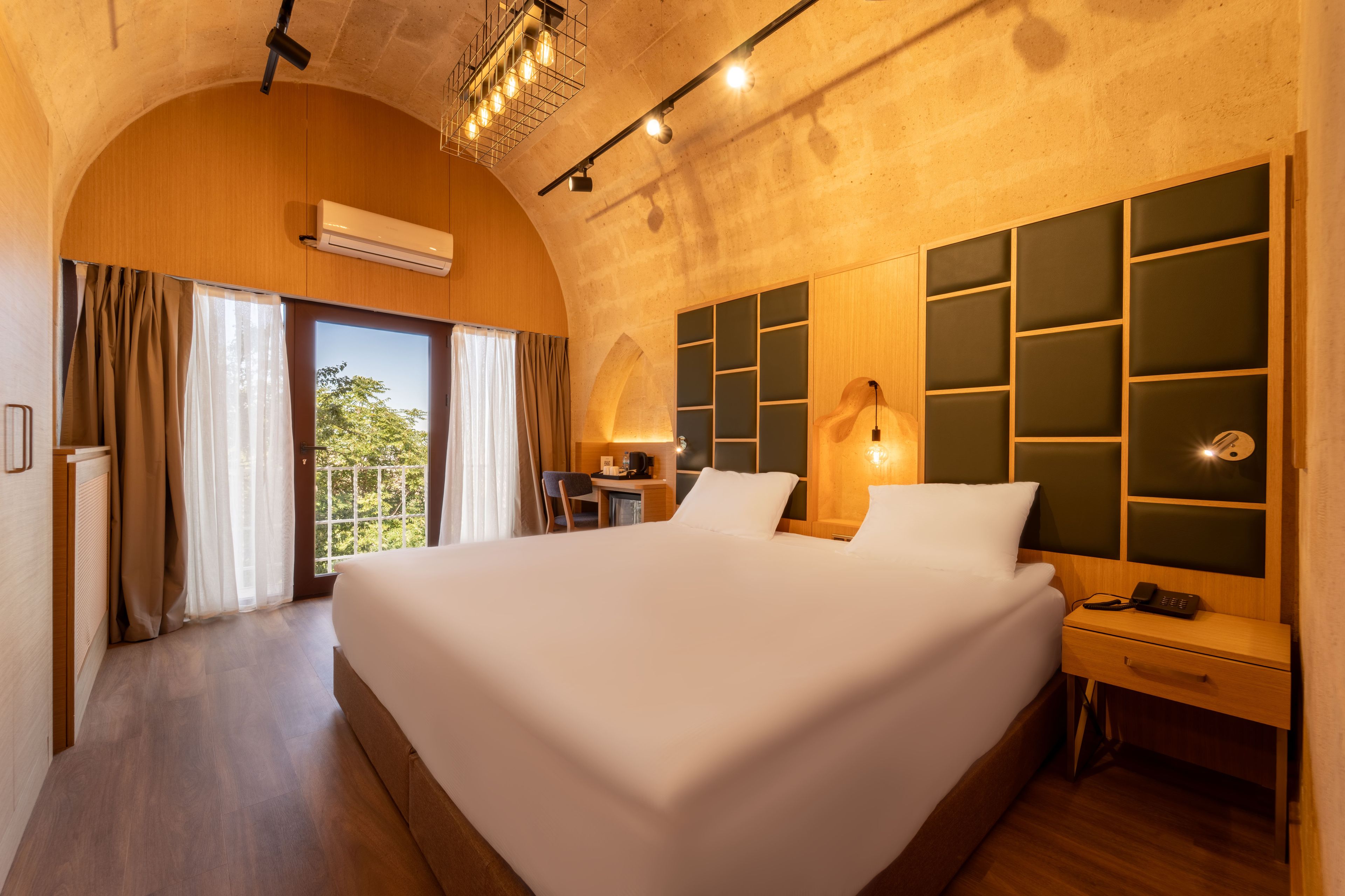 A hotel room with a large bed, a desk, a chair, a nightstand, and a view of the outdoors.
