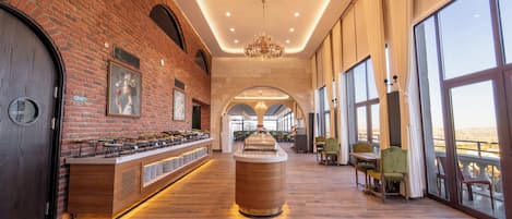 A spacious hotel lobby with a long buffet counter, a large chandelier, and a view through the windows.