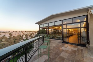 A hotel balcony with a view of the landscape, a seating area with chairs, and a glass door leading to the interior. - Uchisar Kaya Hotel - Special Class (Nevsehir)