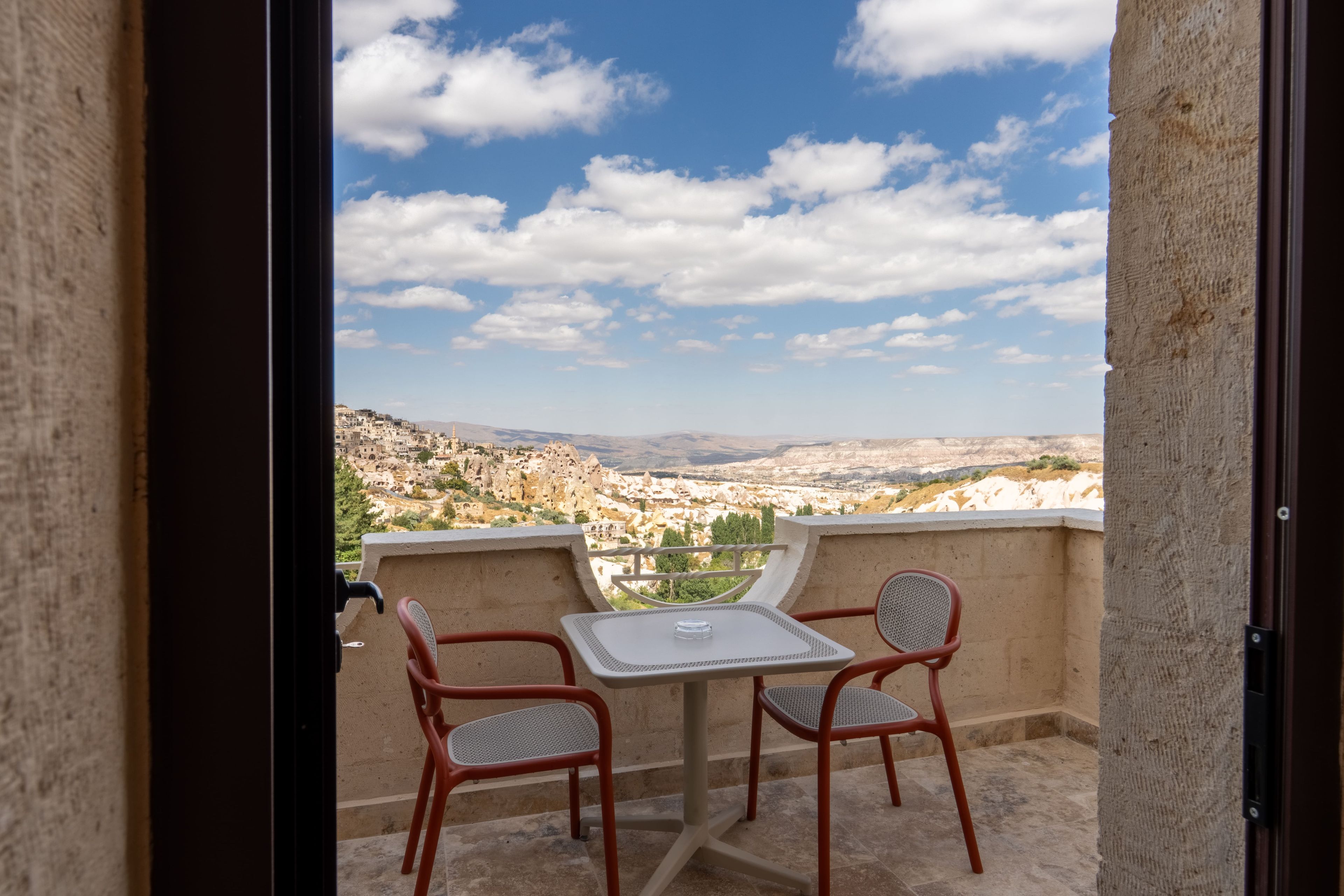 A balcony with a table and two chairs, overlooking a mountainous landscape.