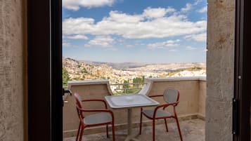 A balcony with a table and two chairs, overlooking a mountainous landscape.